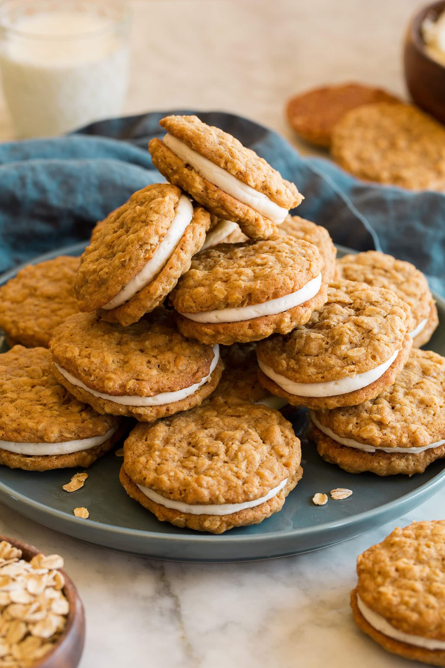 Oatmeal Cream Pies Stack of oatmeal cream pies on a blue plate with a blue cloth do the side and a glass of milk.