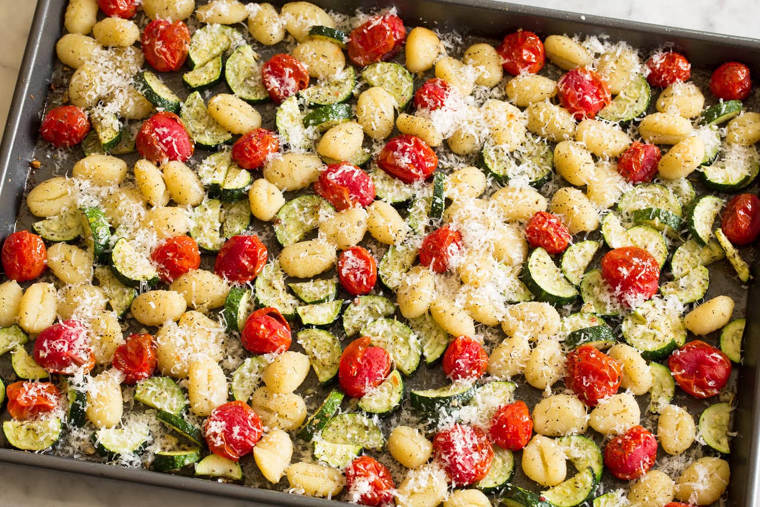 Sheet Pan Gnocchi with Zucchini and Tomatoes Baked sheet pan gnocchi with a parmesan sprinkled over.