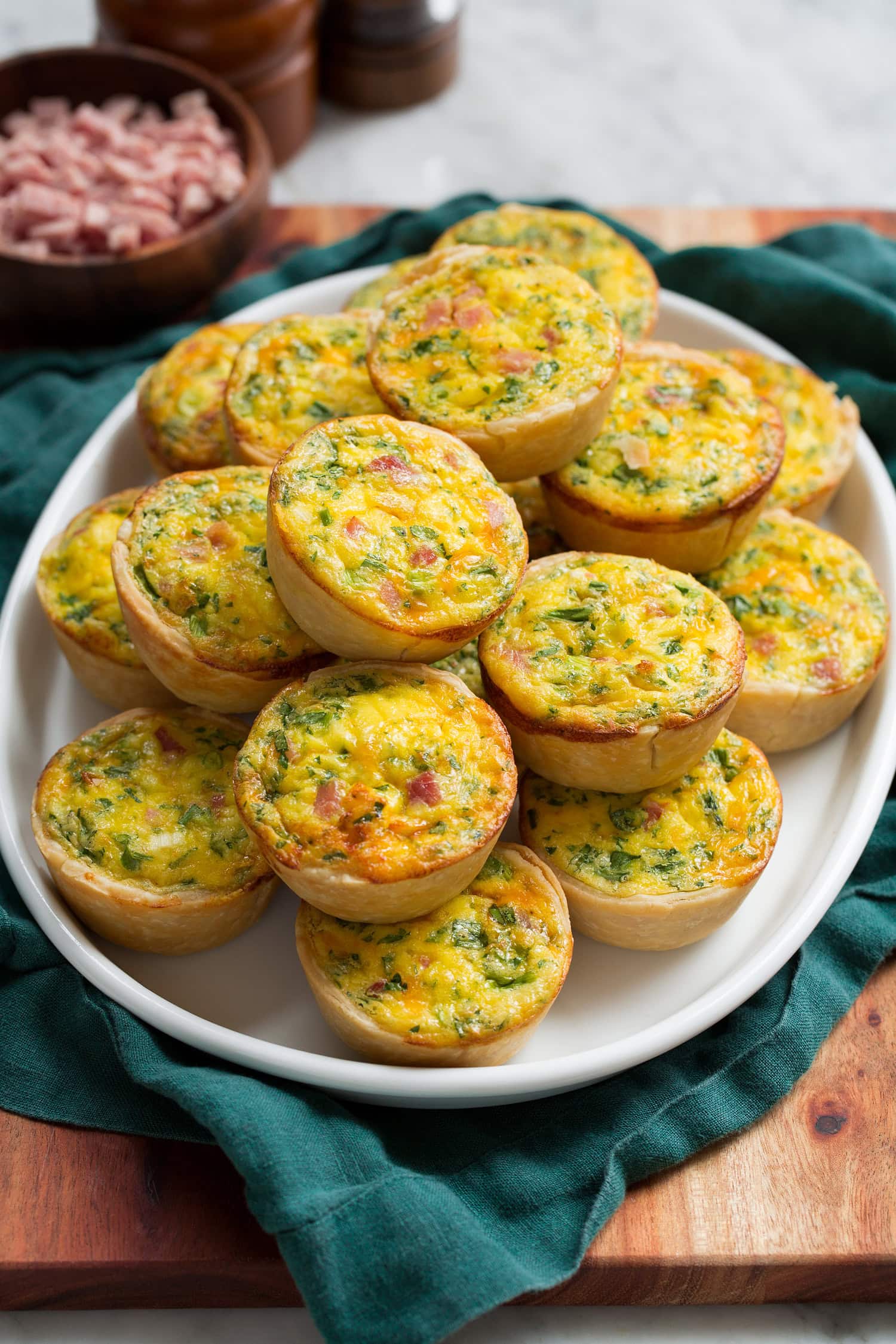 Mini quiche stacked on a white oval platter over a teal cloth.