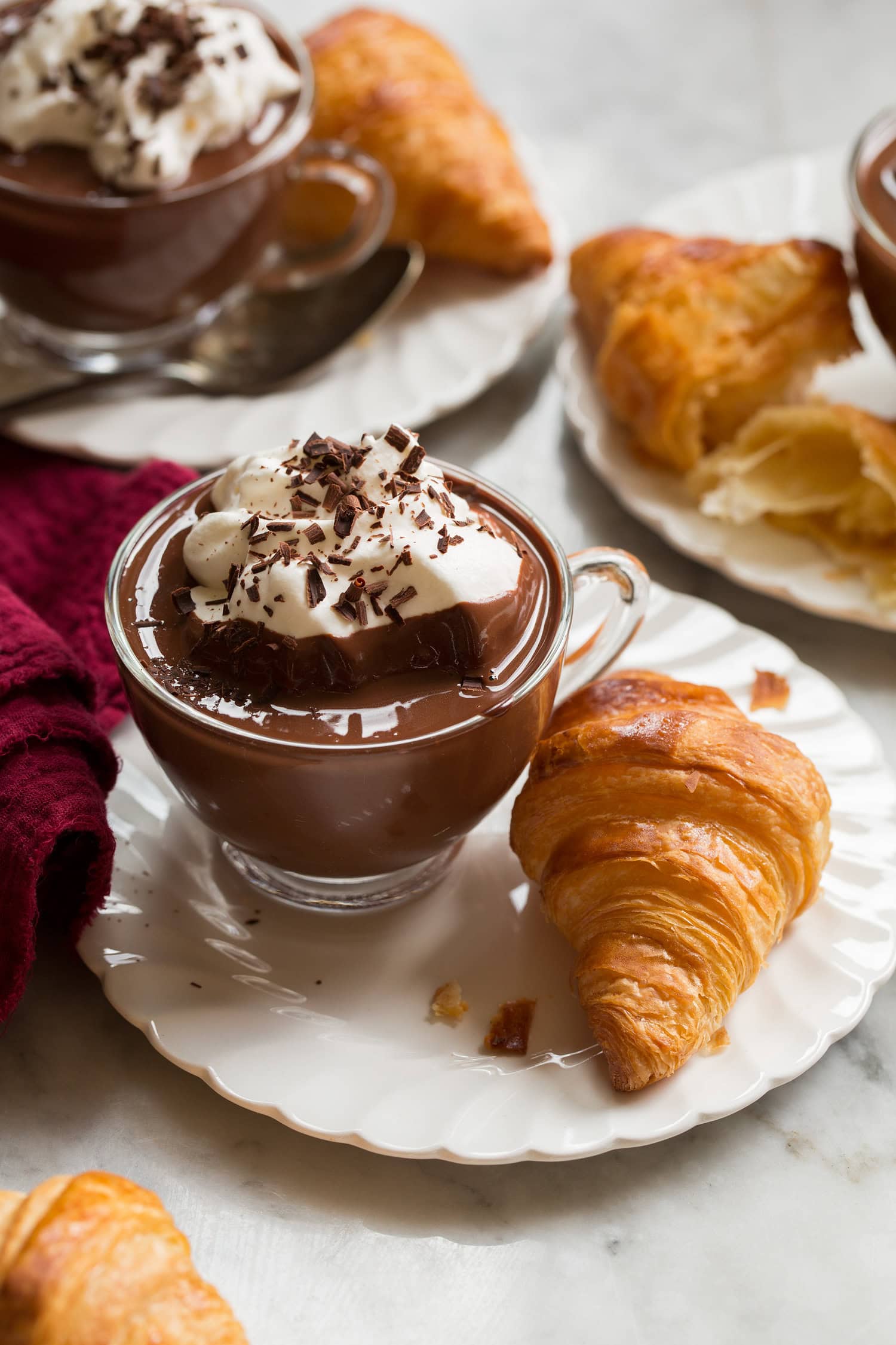 French hot chocolate in a small glass mug served with a croissant on the side.