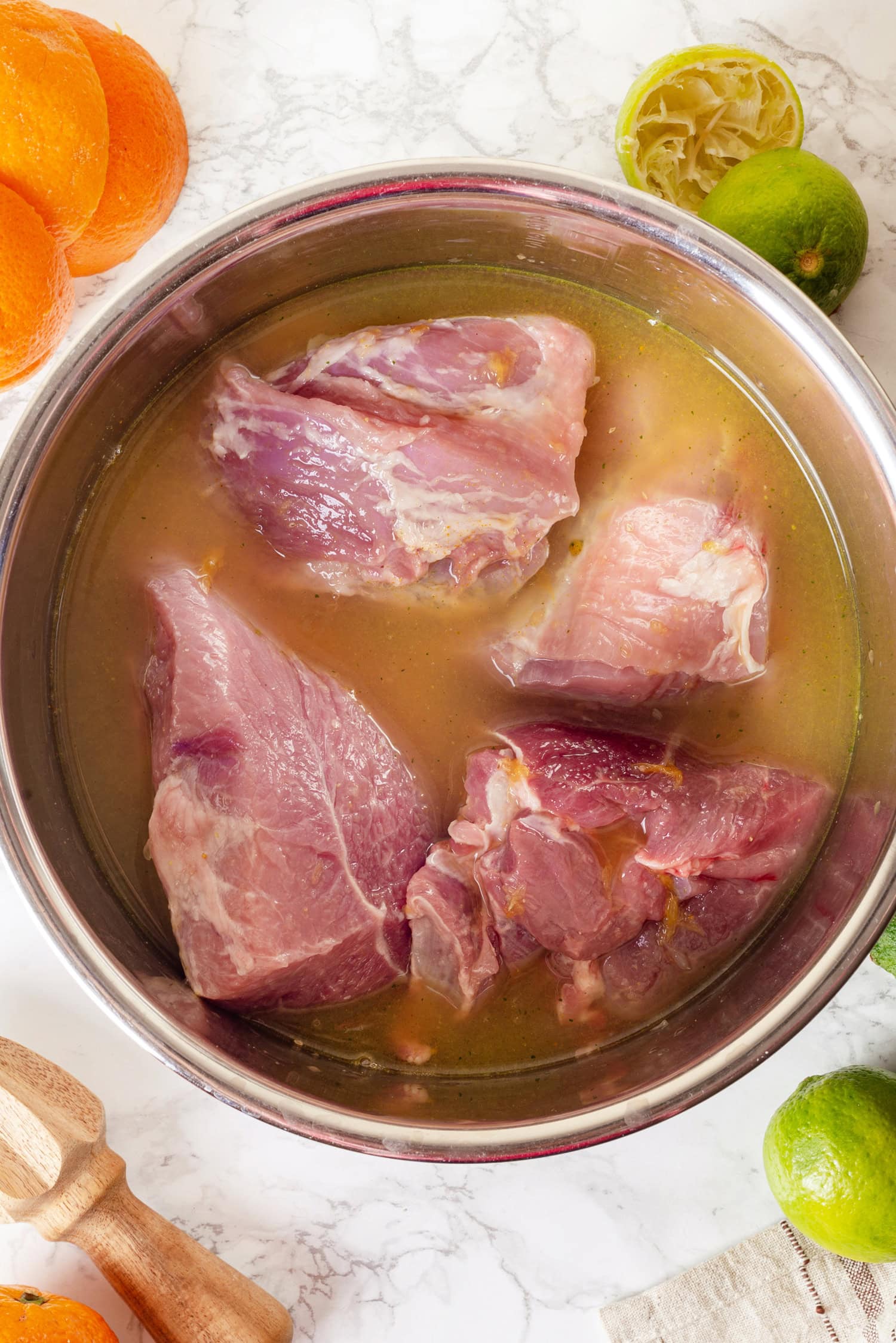 Pork chunks in liquid in a stainless bowl.