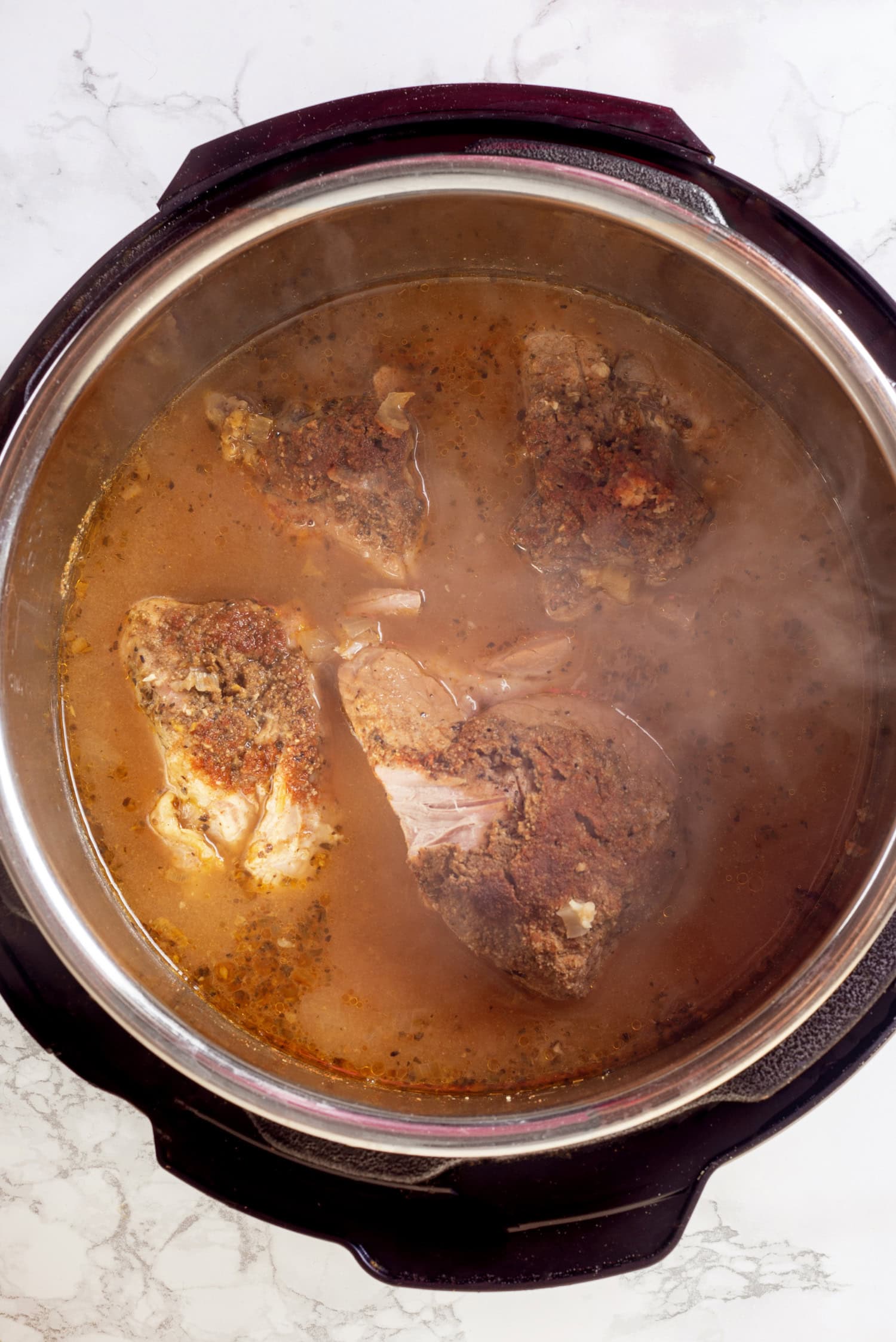 Carnitas finished cooking, shown steaming in the cooking broth.