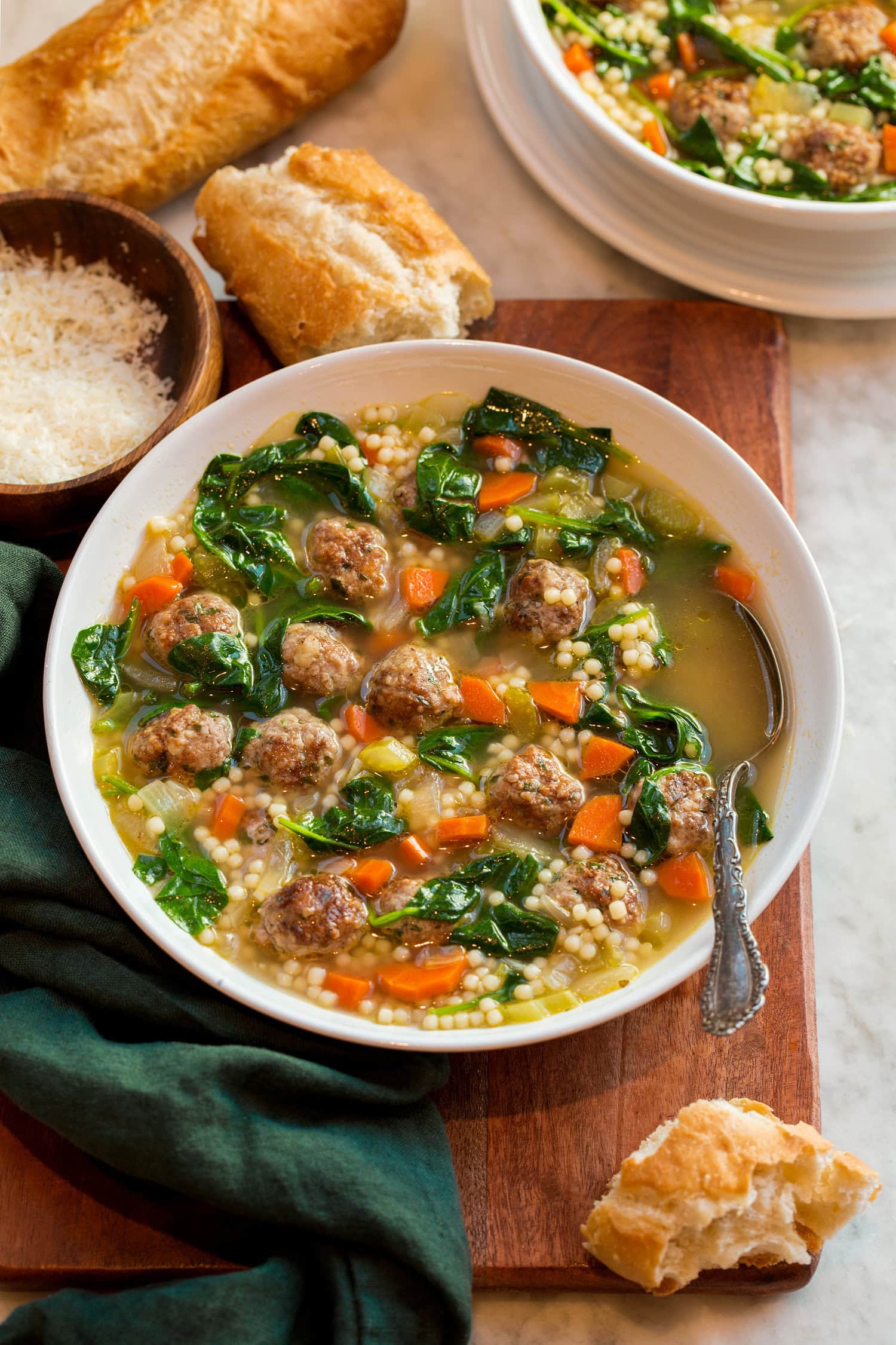 Italian Wedding Soup Italian wedding soup in a serving bowl with baguette bread and parmesan shown for serving.