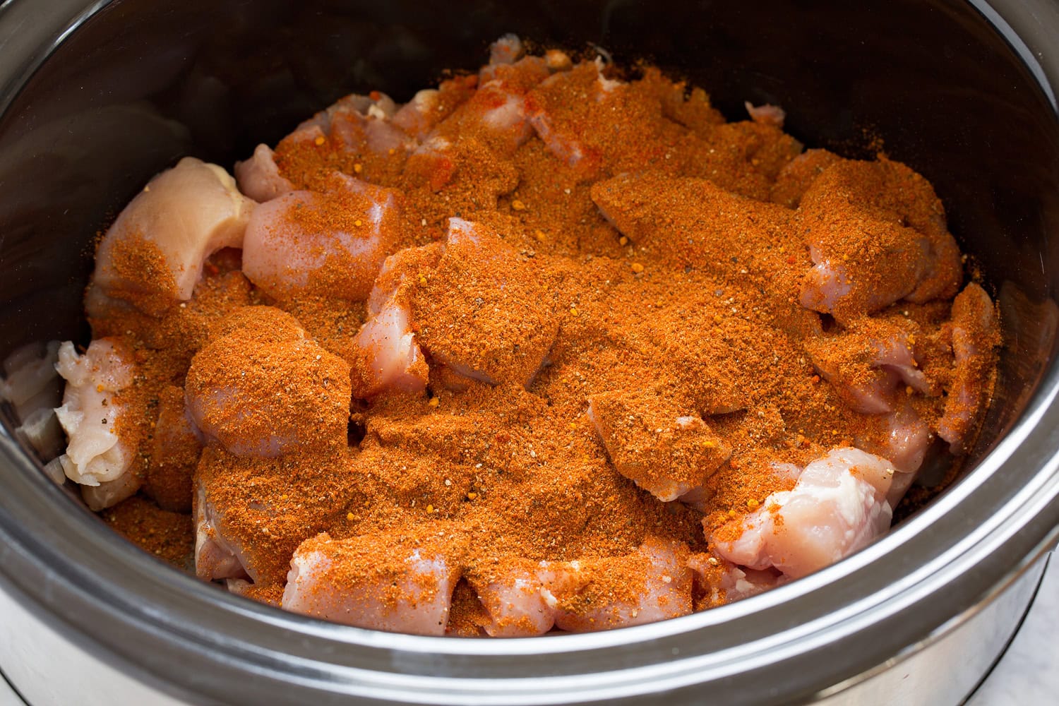 Slow Cooker Chicken Tikka Masala Spices added over chicken thigh chunks in crock pot.