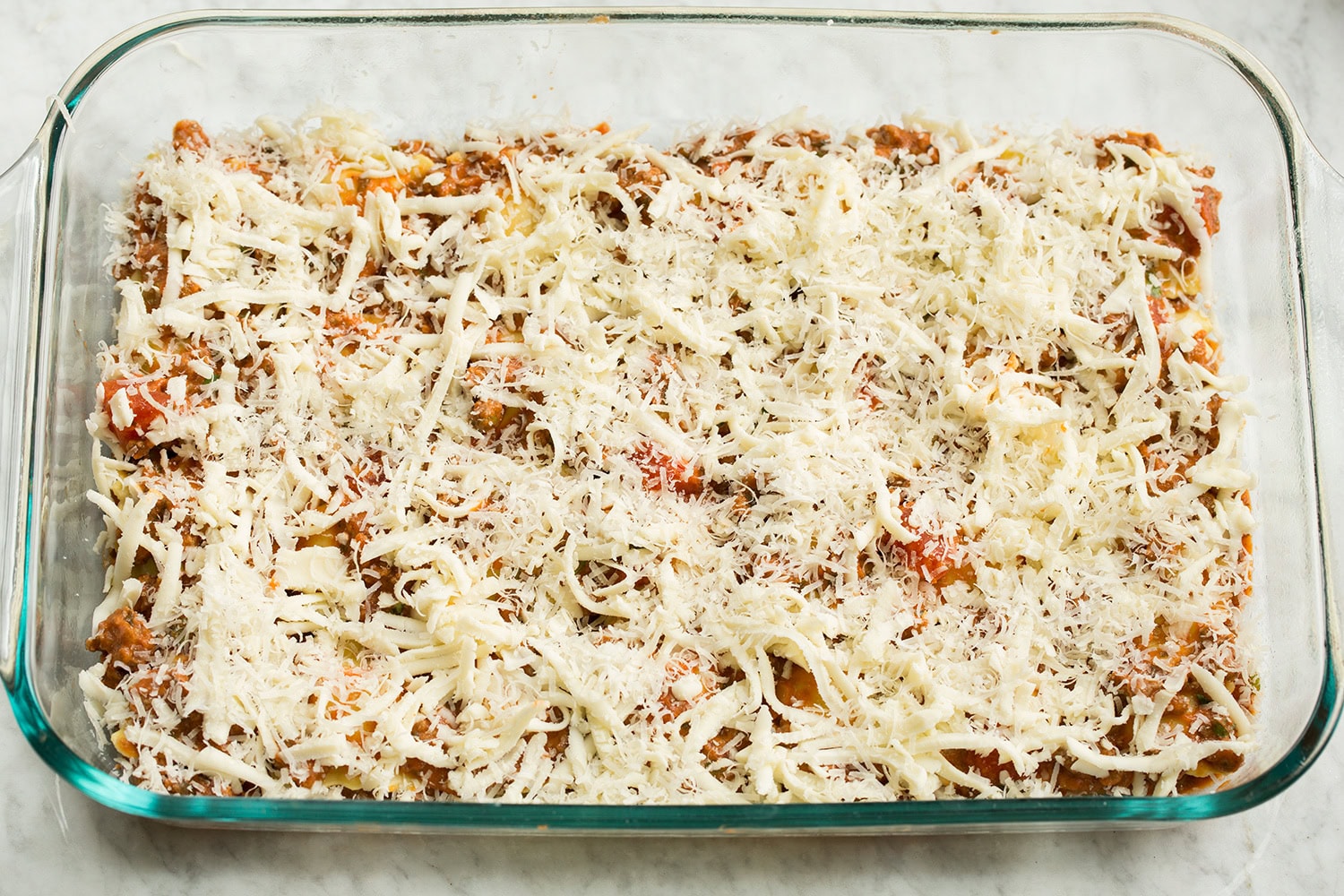 Shredded cheeses added over sauce layer