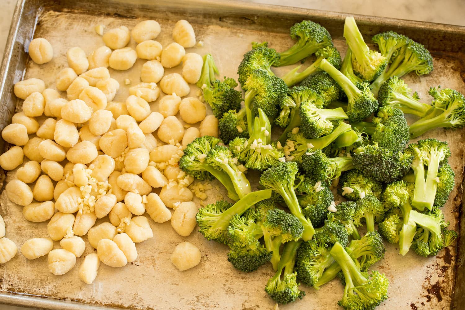 Broccoli, gnocchi, garlic and olive oil on sheet pan before tossing.