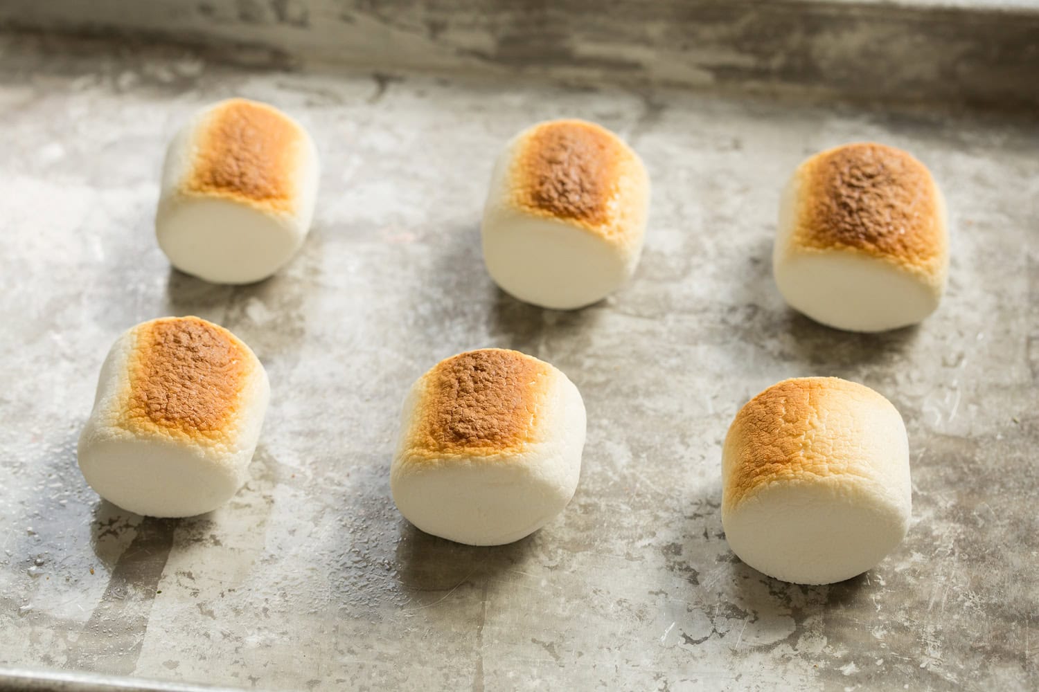 Oven S'mores Six toasted marshmallows on baking sheet after broiling on one side.