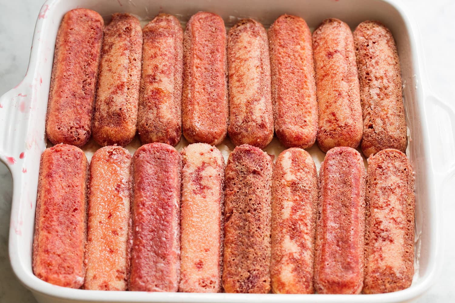 Strawberry Cheesecake Tiramisu Juice soaked lady fingers in ceramic baking dish.