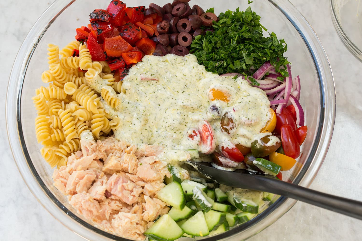 Tuna Pasta Salad Pasta salad ingredients including tuna, vegetables, olives and creamy dressing in a bowl shown before mixing.