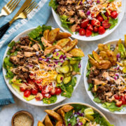 Four burger bowls shown from overhead on a marble surface with a blue cloth to the side.