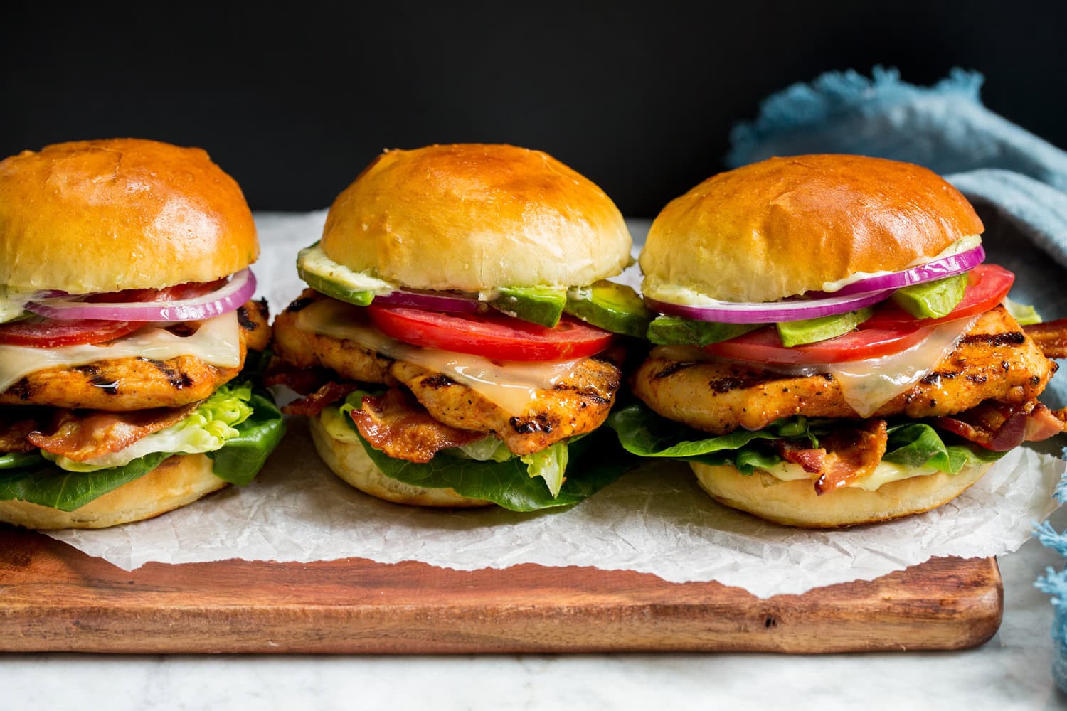 Grilled Chicken Sandwiches Three grilled chicken sandwiches on a cutting board with parchment paper.