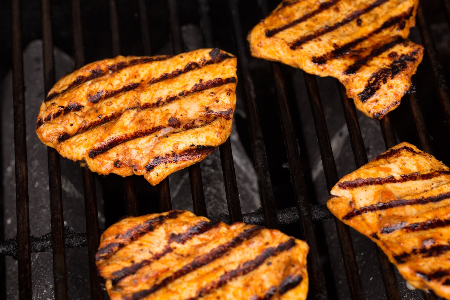 Grilled Chicken Sandwiches Four small flattened chicken breasts shown on the grill with grill marks on them.