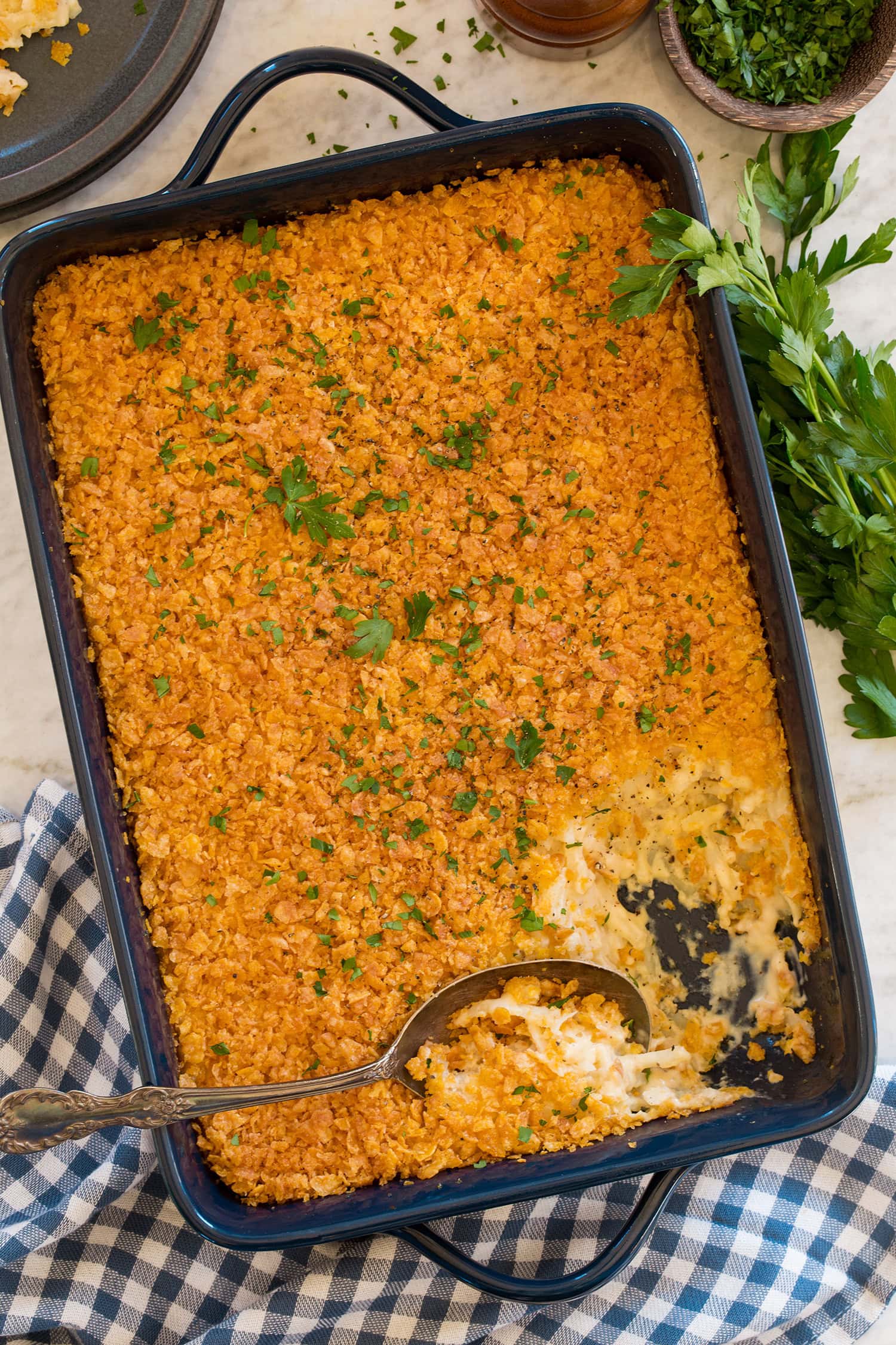 Funeral potato casserole in a navy baking dish with a scoopful removed to show interior.