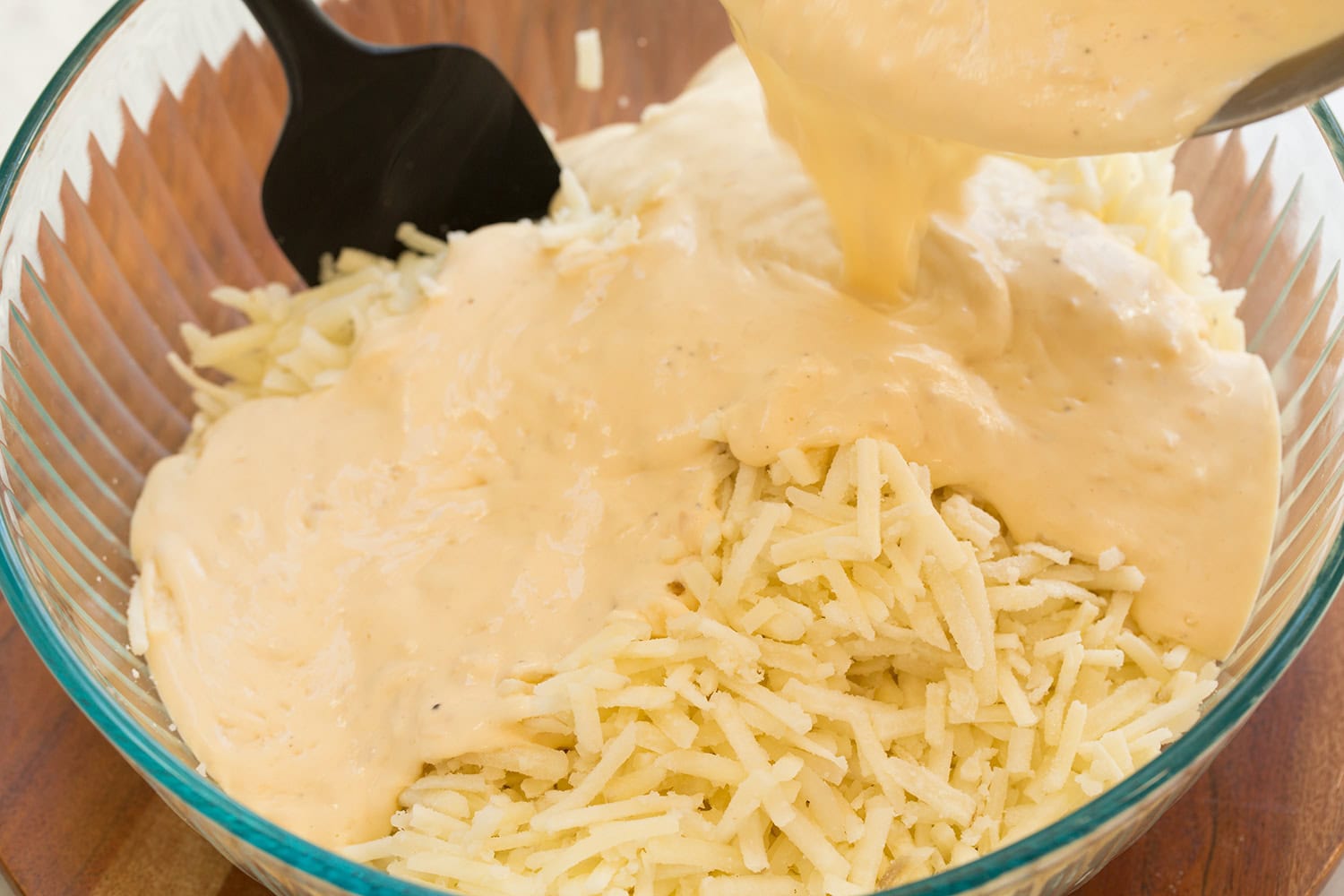 Cheese sauce poured over hash browns in glass mixing bowl.
