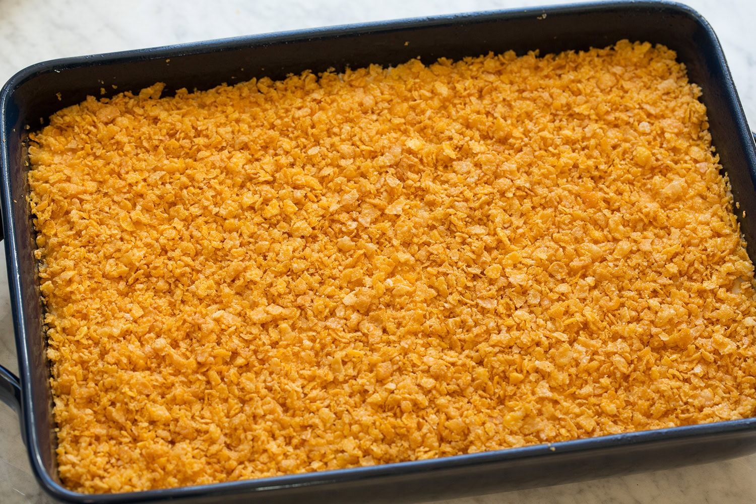 Cornflake topping spread over hash brown mixture in baking dish.