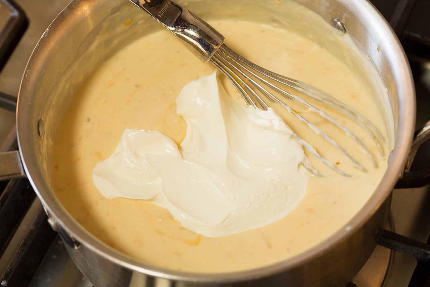 Sour cream added to sauce in saucepan.