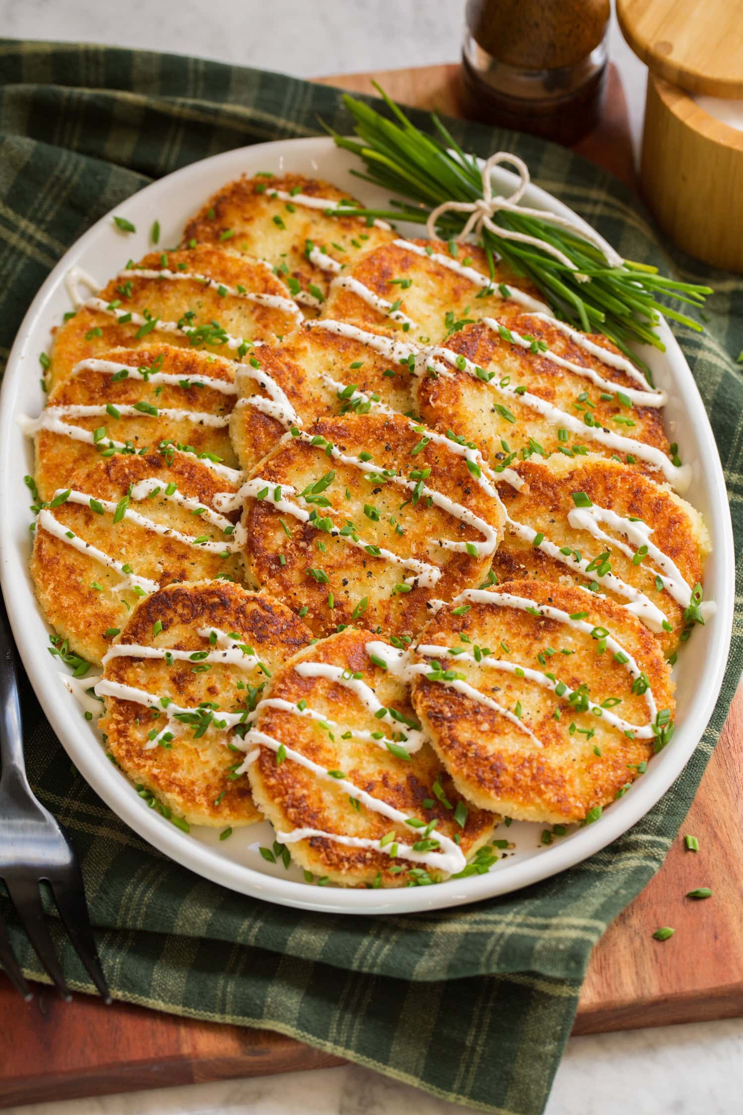 Potato cakes on a white oval platter over a green gingham cloth.