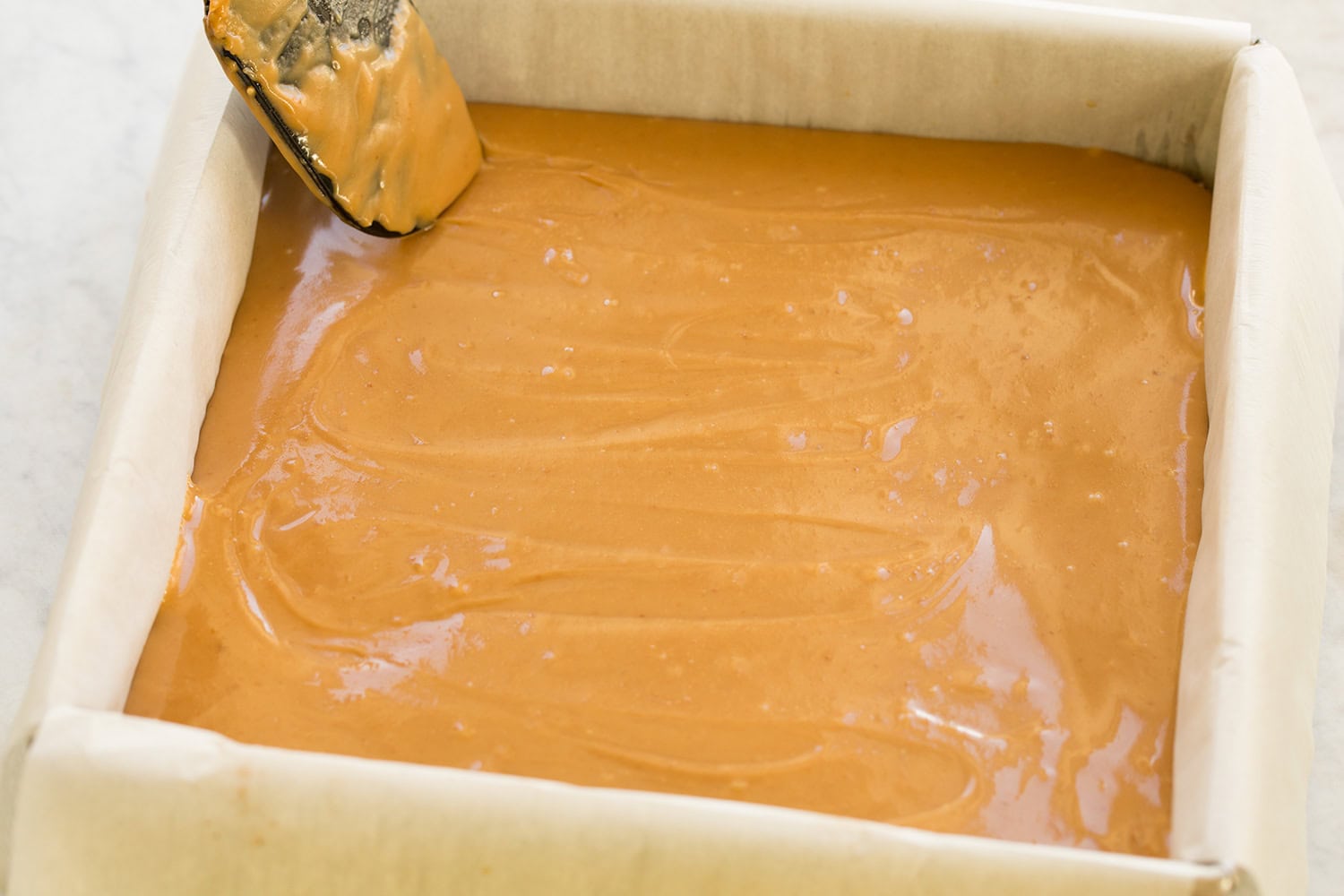 Caramel being spread over shortbread layer.