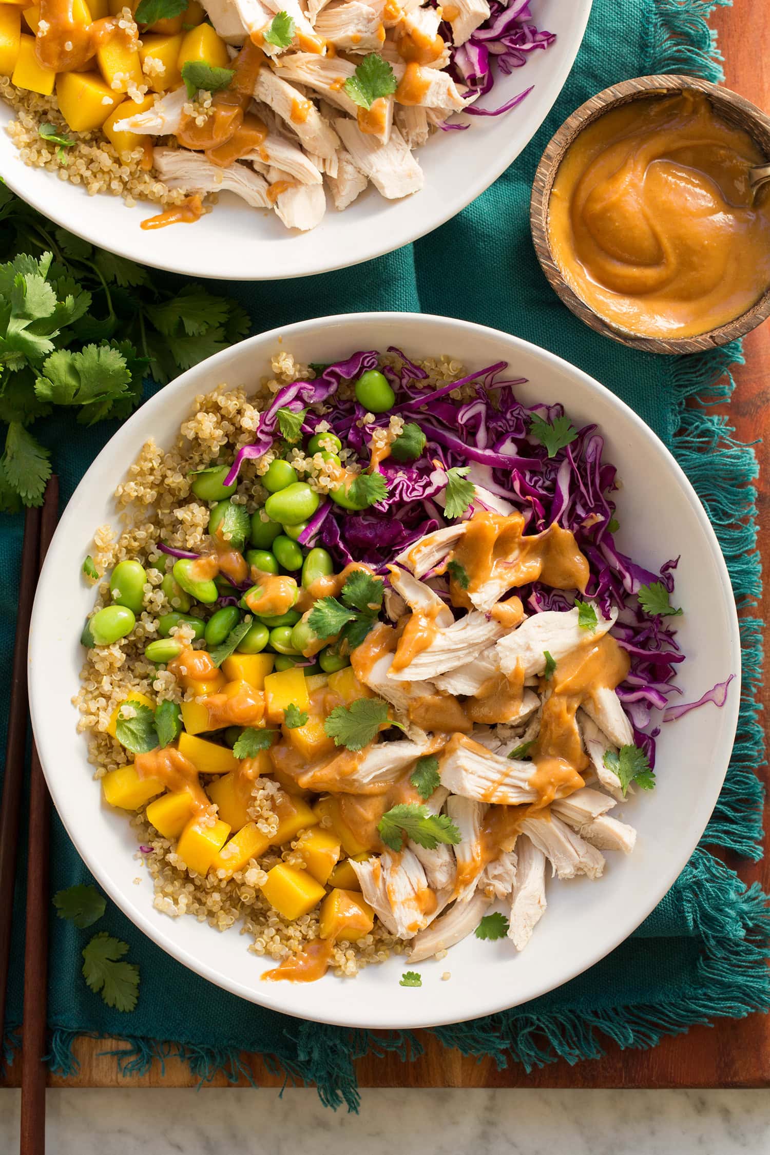 Overhead photo of a protein bowl with quinoa, rotisserie chicken, edamame, cabbage, mango and peanut sauce.