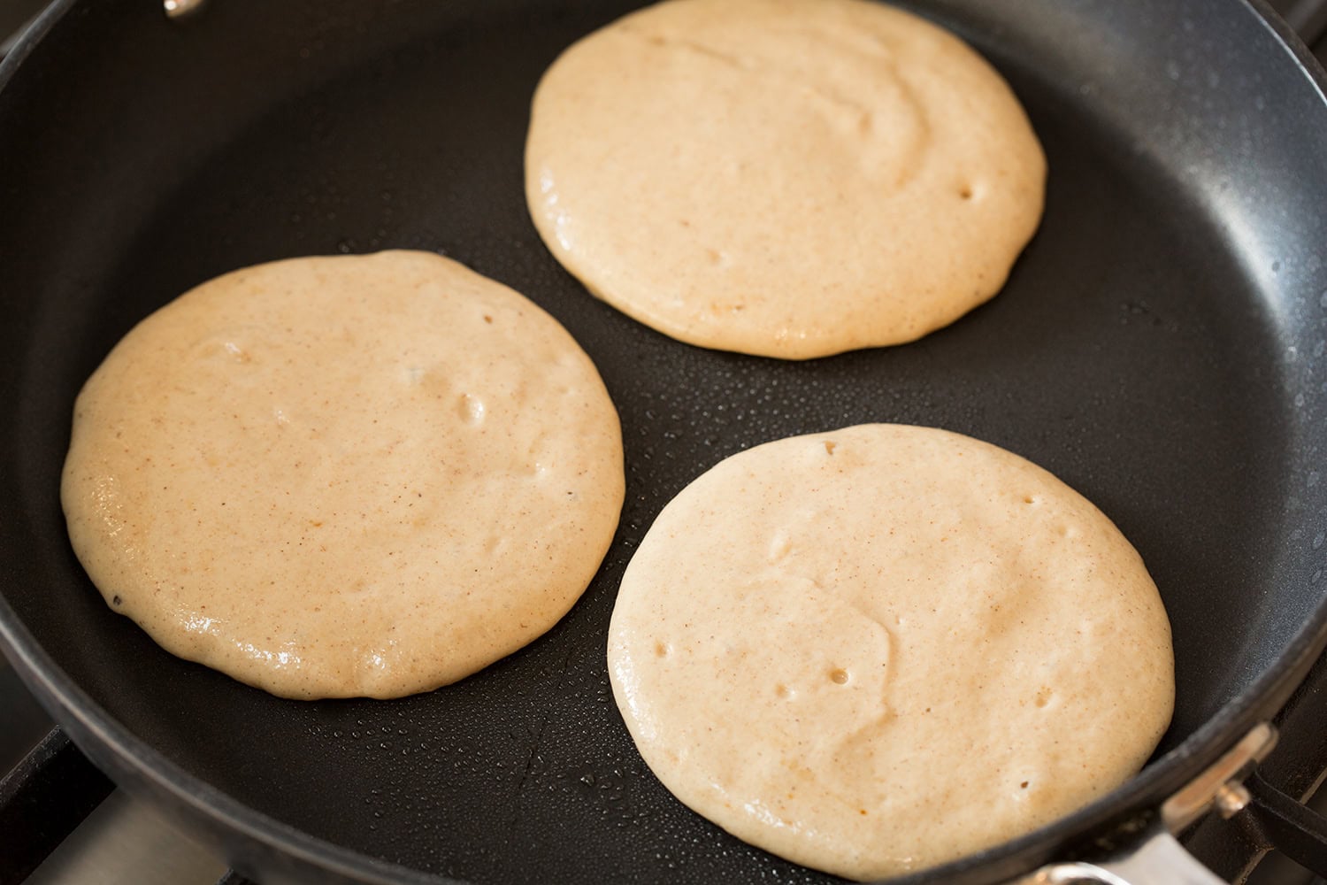 Protein pancakes cooking in a 12-inch non-stick skillet on first side.
