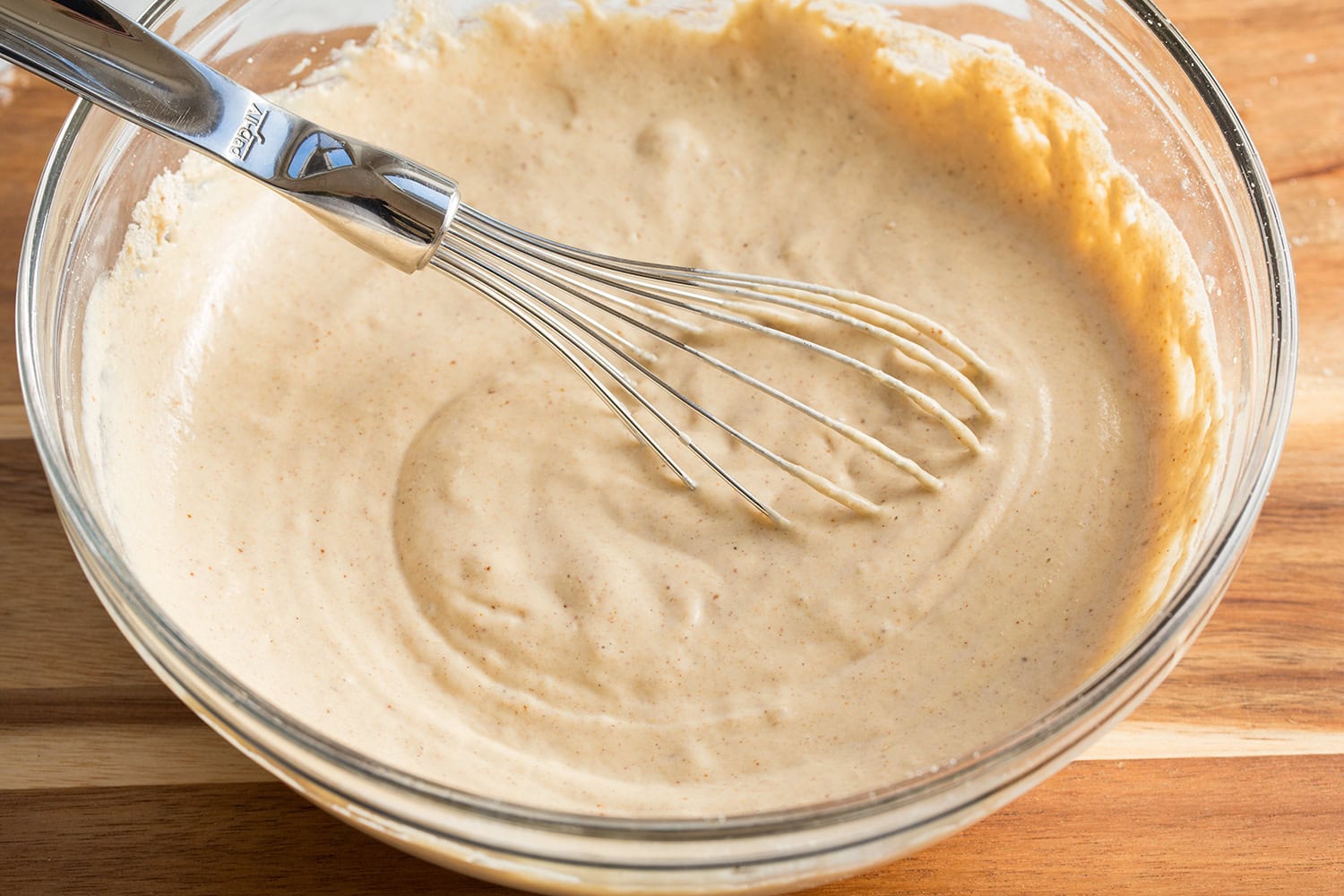 Protein pancake batter in a glass mixing bowl with a whisk.