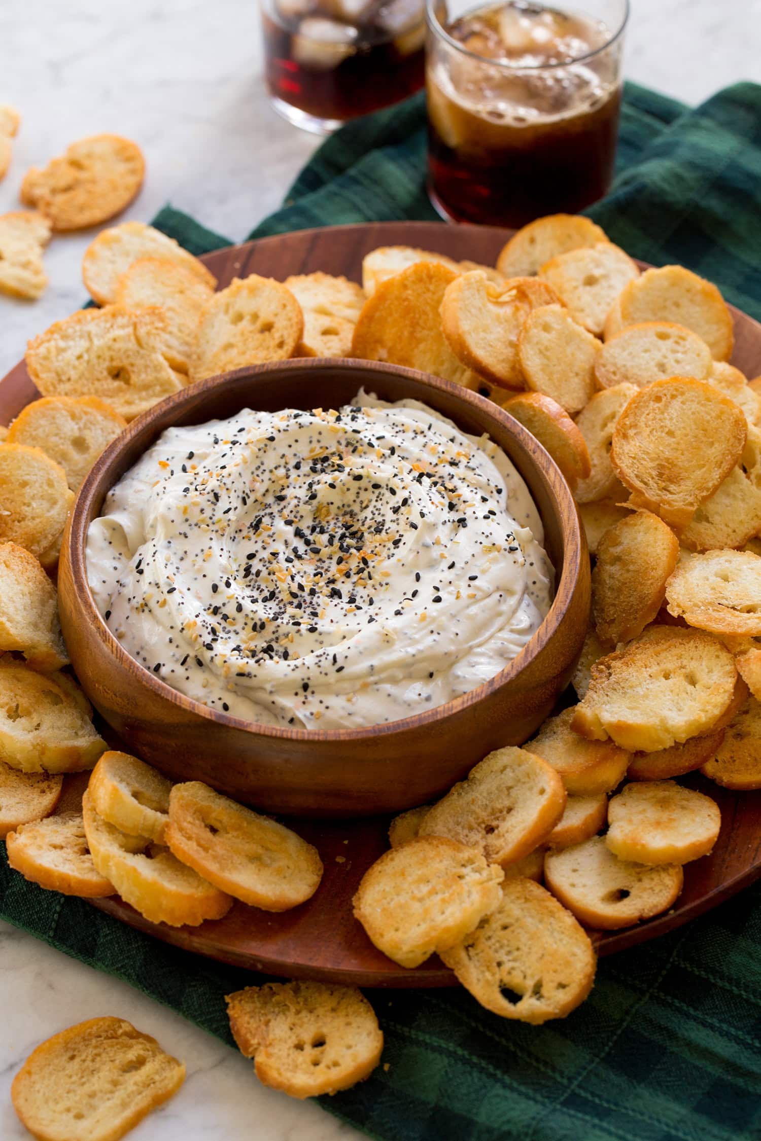 Everything bagel cream cheese dip with bagel chips on a wooden platter.