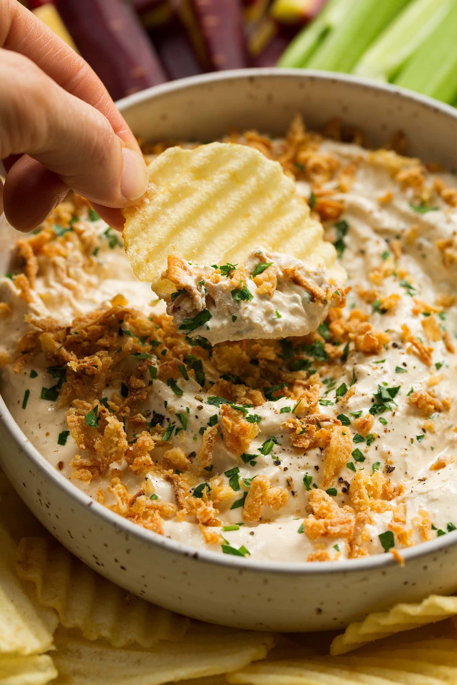 Close up photo of potato chip being dipped in homemade French onion dip.