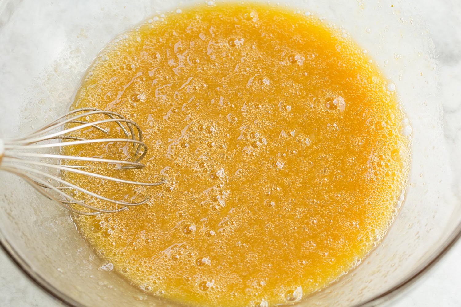 Egg, oil and applesauce mixture shown blended in glass dish.