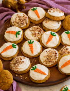 Carrot cake cookies on a wooden platter shown with a purple cloth and bunny decorations to the side.