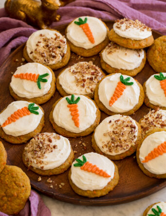 Carrot cake cookies on a wooden platter shown with a purple cloth and bunny decorations to the side.