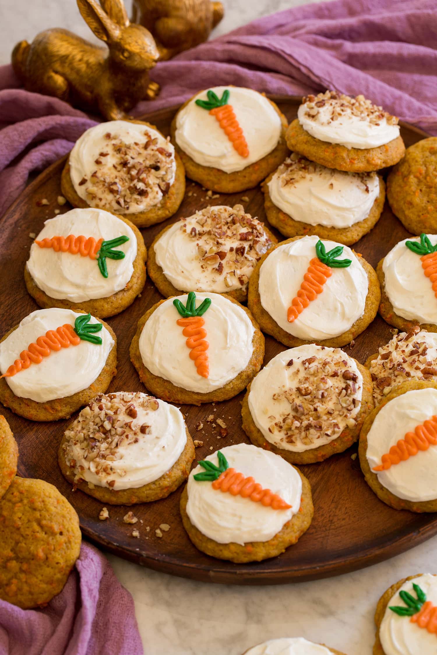Carrot cake cookies on a wooden platter shown with a purple cloth and bunny decorations to the side.