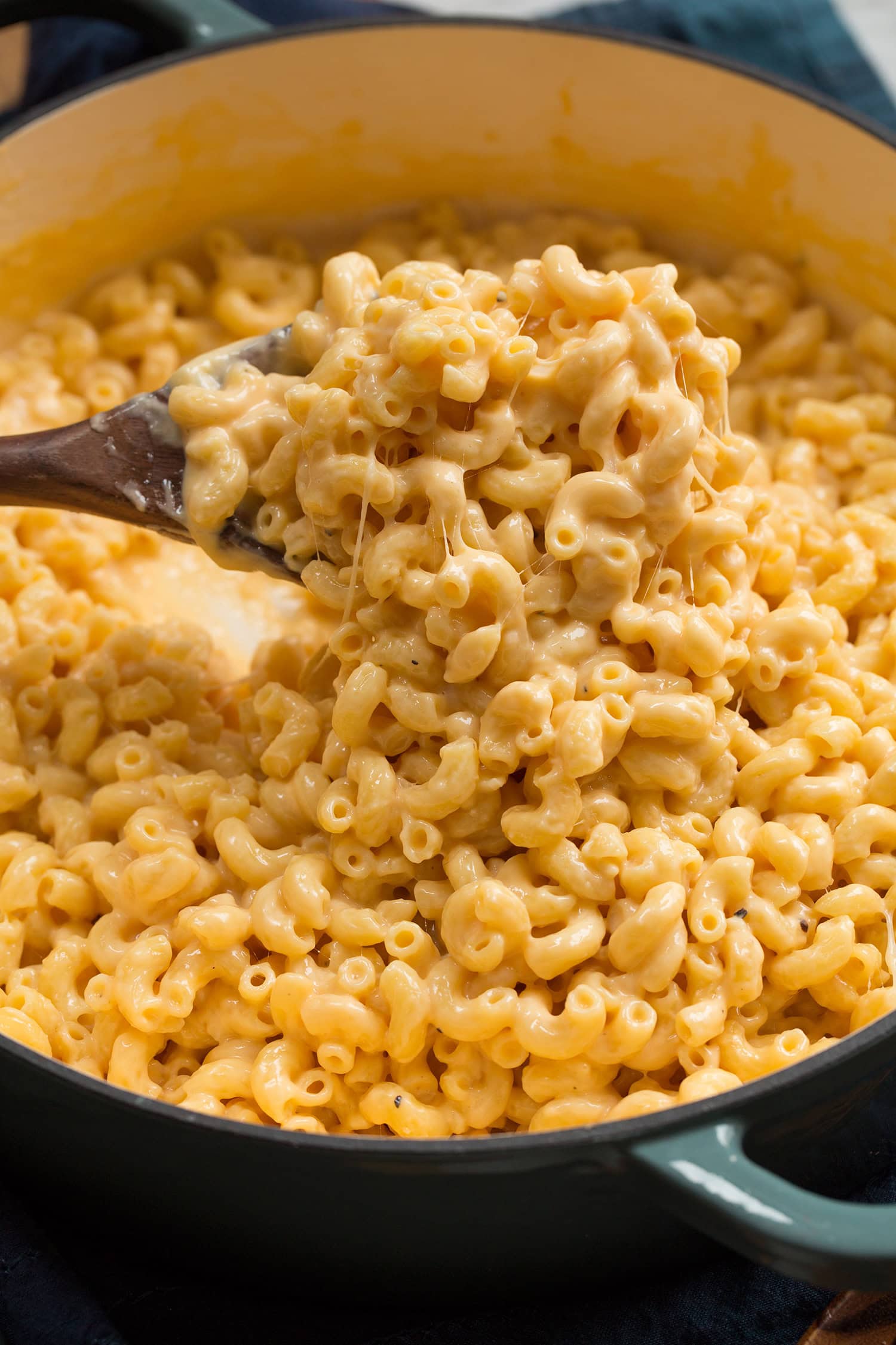 Close up photo of mac and cheese scooped out on a wooden spoon. Shows thick creamy texture of sauce and stringy cheese.