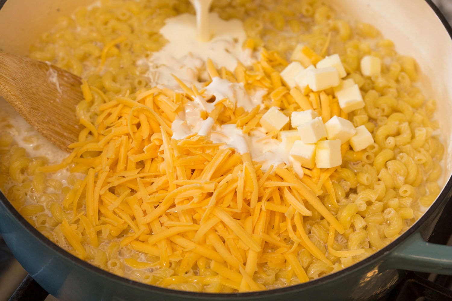 Cream butter and American cheese added to cooked pasta in pot.