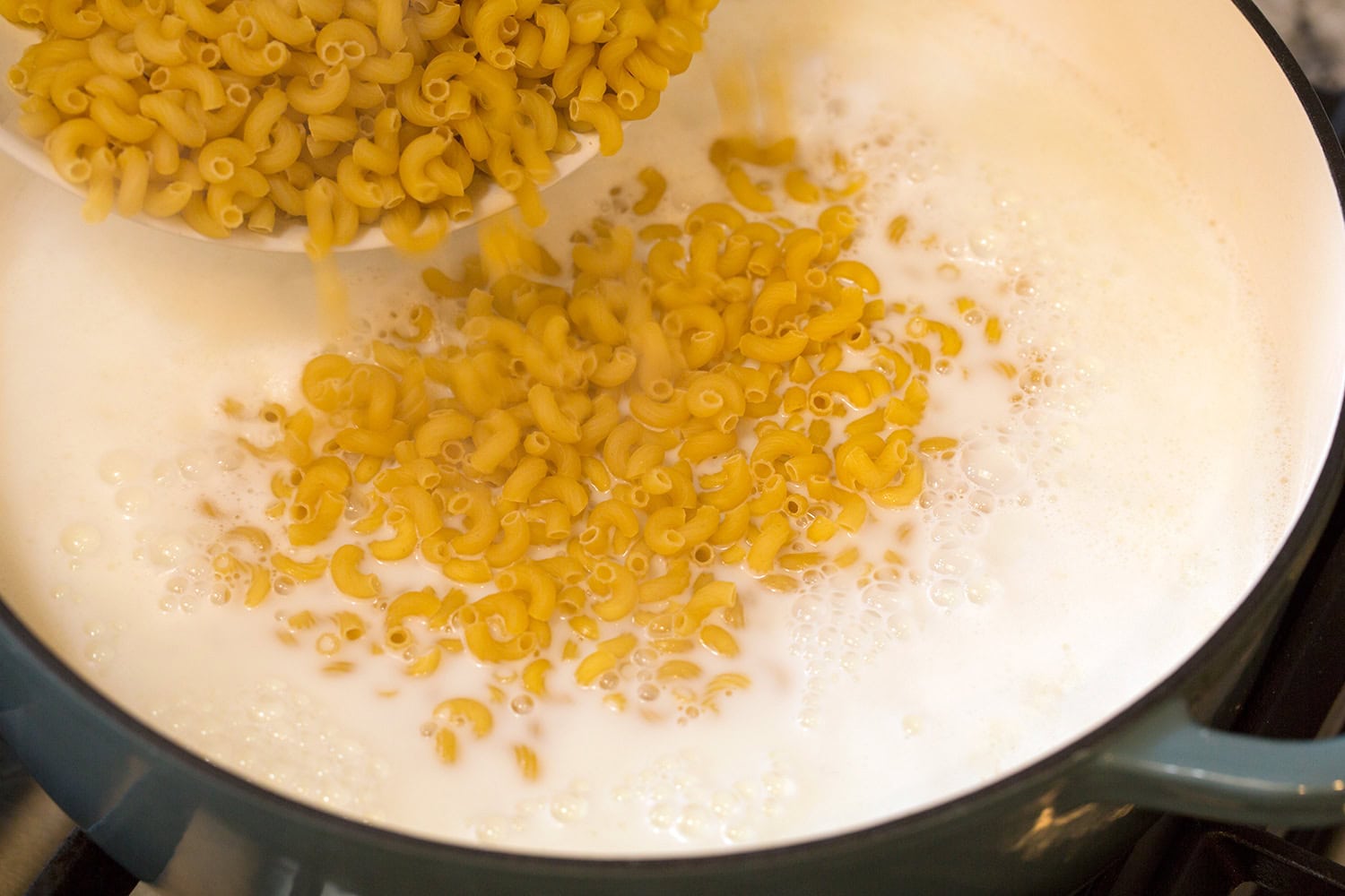 Elbow macaroni noodles added to boiling milk and water in pot.