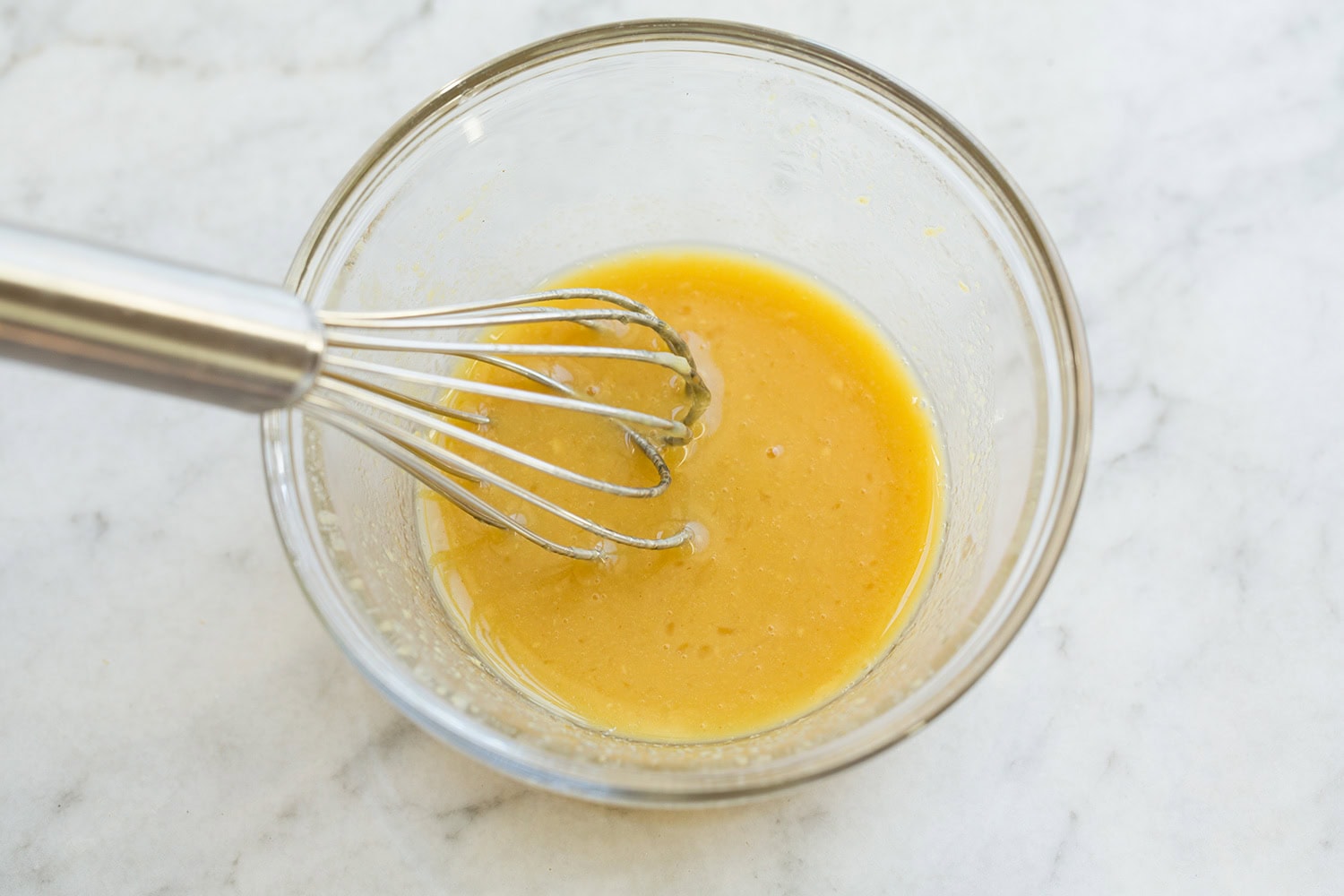 Honey, dijon mustard and lemon mixed in a small glass mixing bowl.