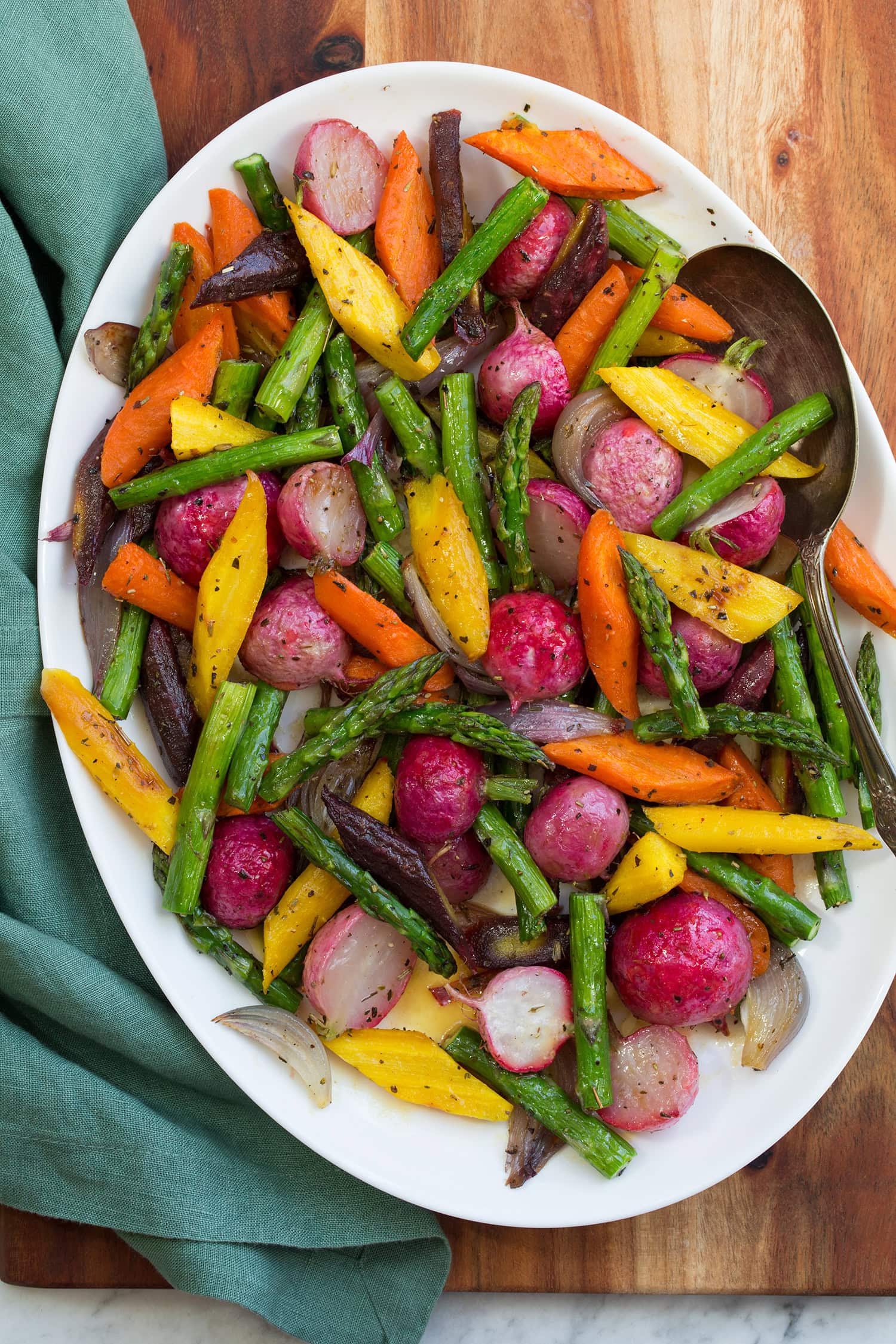 Roasted radishes, rainbow carrots, asparagus and shallot on white platter.