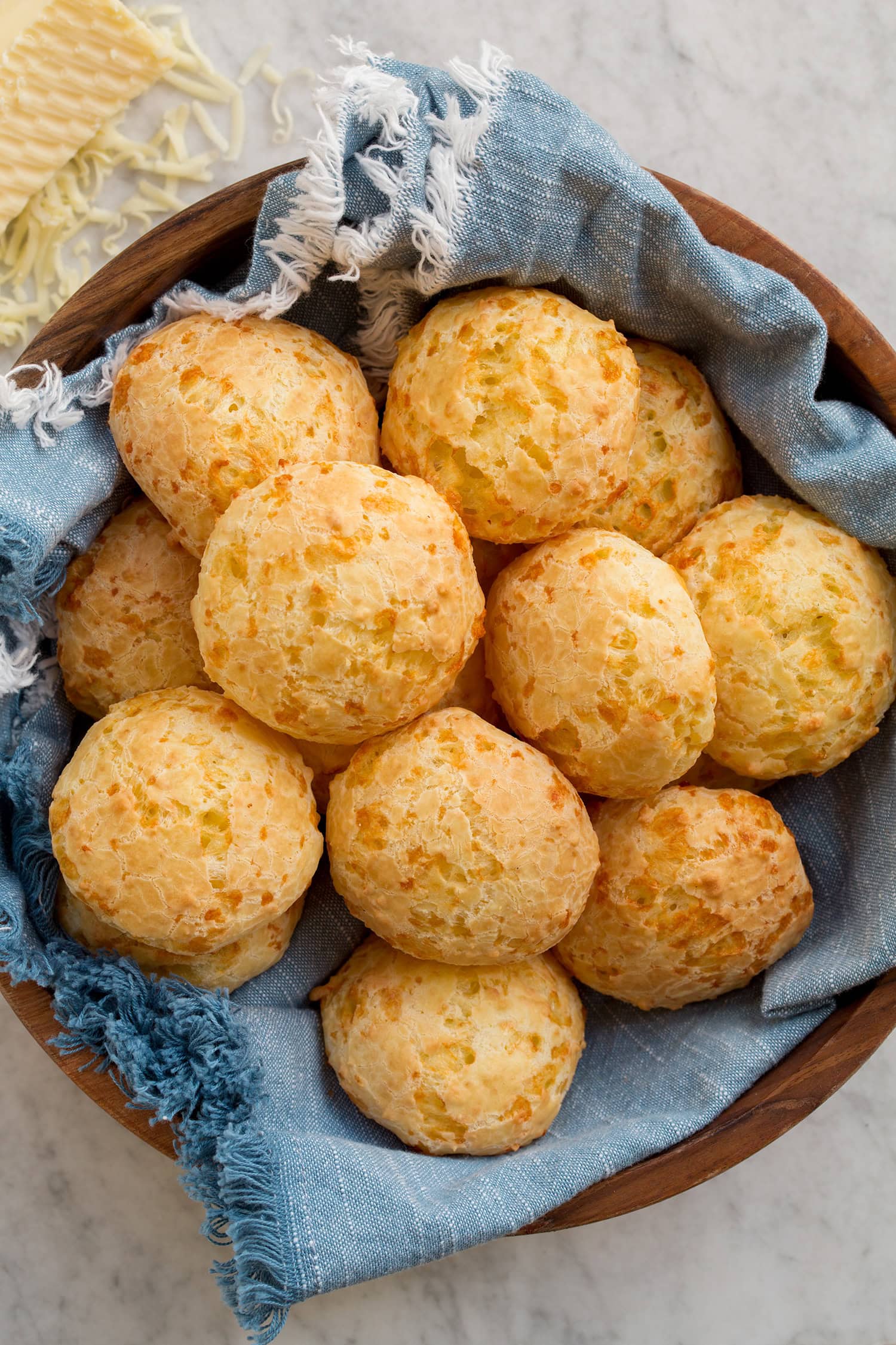 Brazilian Cheese Bread (Pão de Queijo) Overhead photo of pao de gueijo bread in a bowl with a blue cloth.