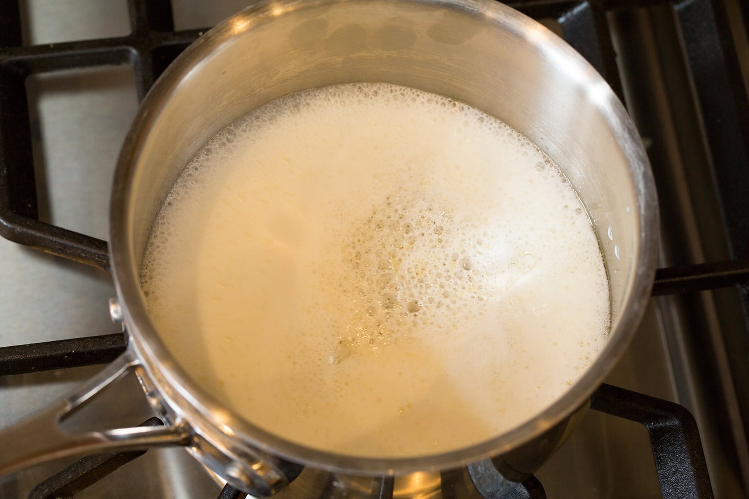 Brazilian Cheese Bread (Pão de Queijo) Milk and avocado oil heating in a small stainless steel saucepan on the stovetop.
