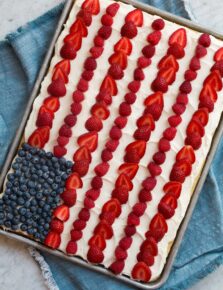 American flag cake made in a sheet pan. Shown topped with frosting, sliced strawberries, blueberries and raspberries.