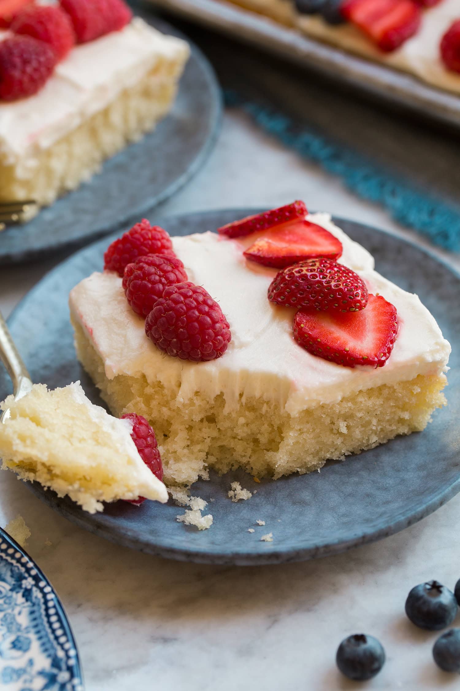 Close up photo of a slice of a vanilla sheet pan cake with fresh fruit on top.