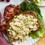 Honey mustard chicken salad shown on a slice of rye bread with bacon and lettuce to the side.