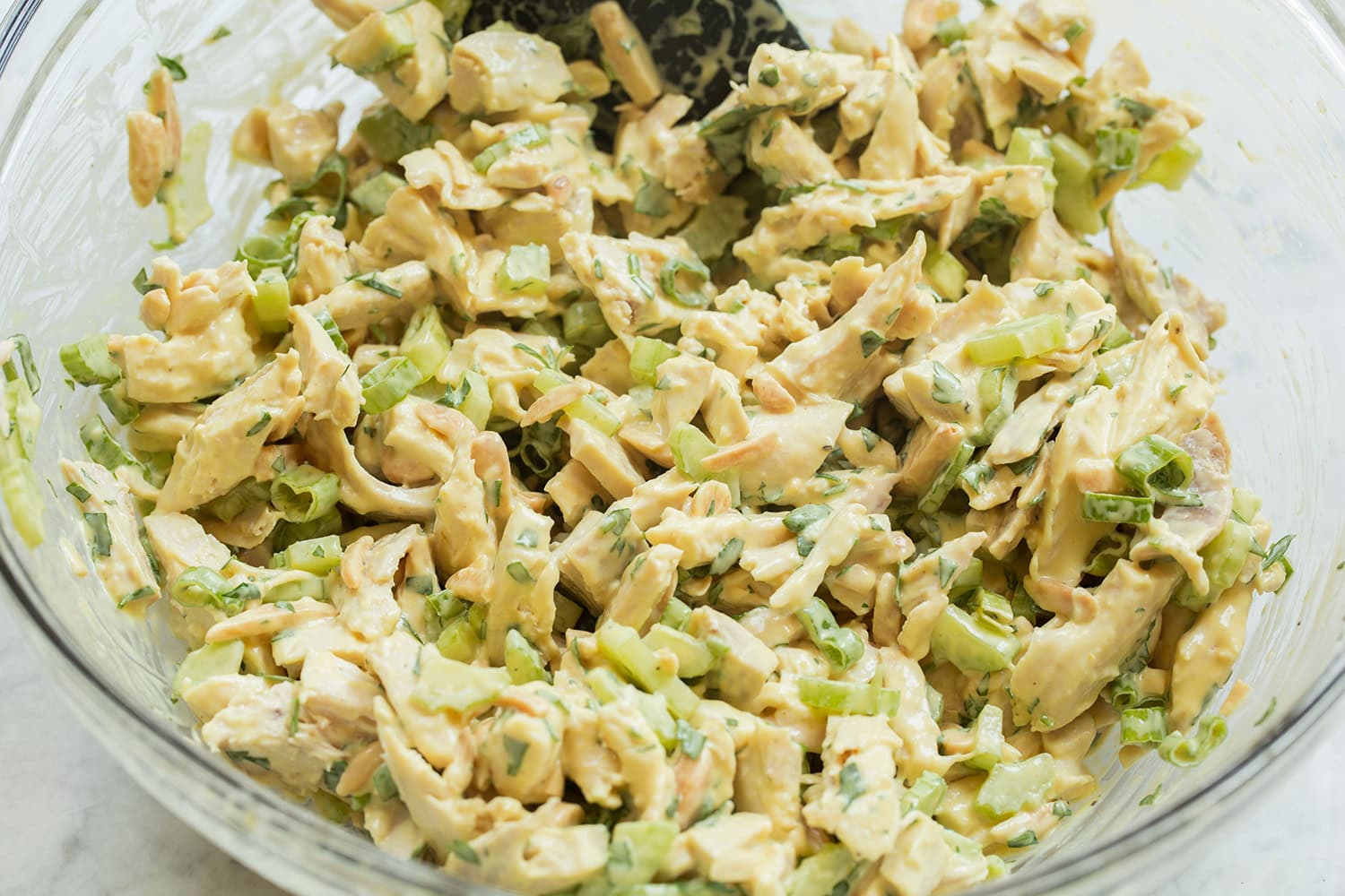 Chicken salad shown in a glass mixing bowl after tossing with dressing.