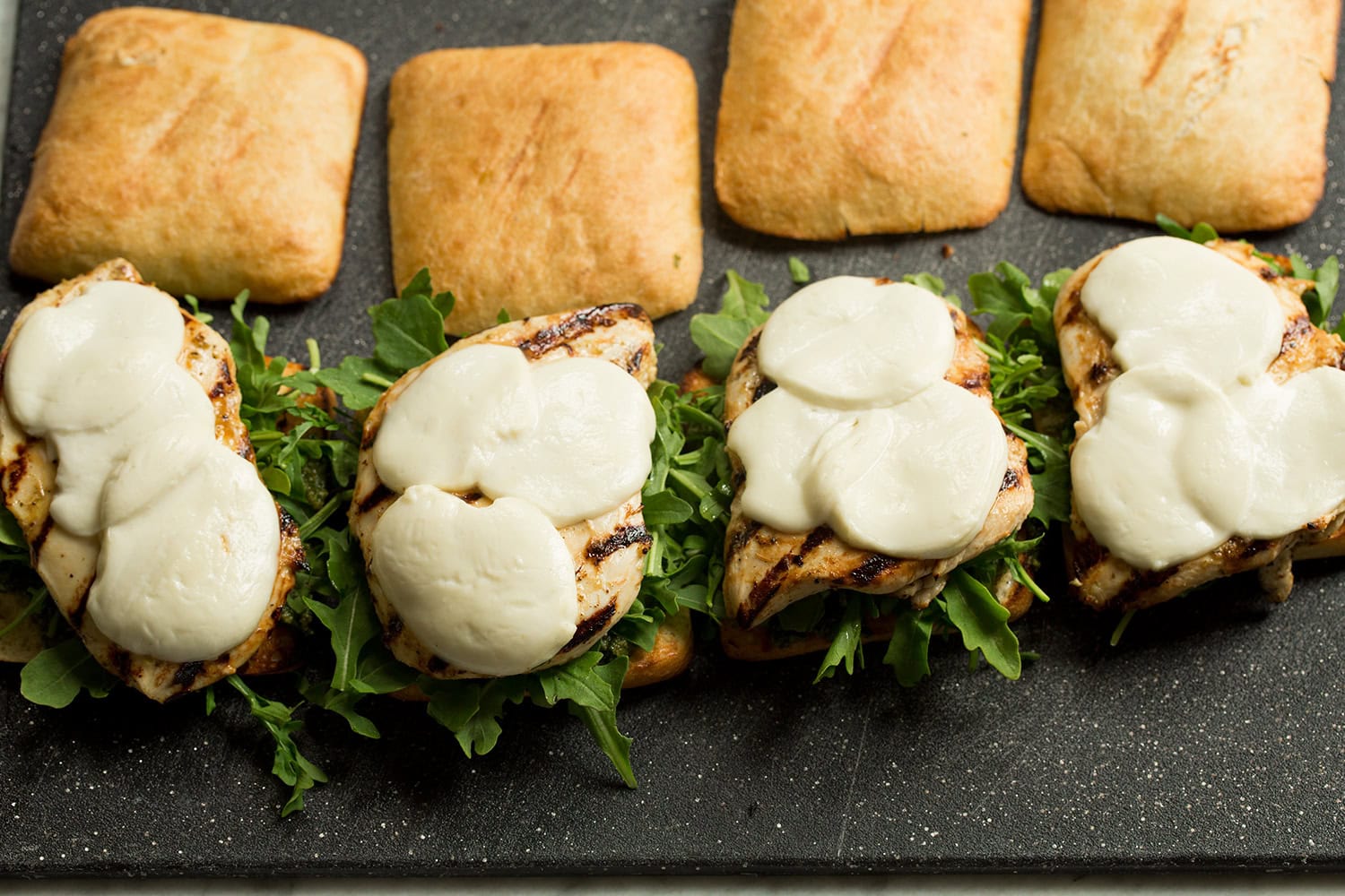 Grilled chicken breast with melted fresh mozzarella placed over sandwiches.