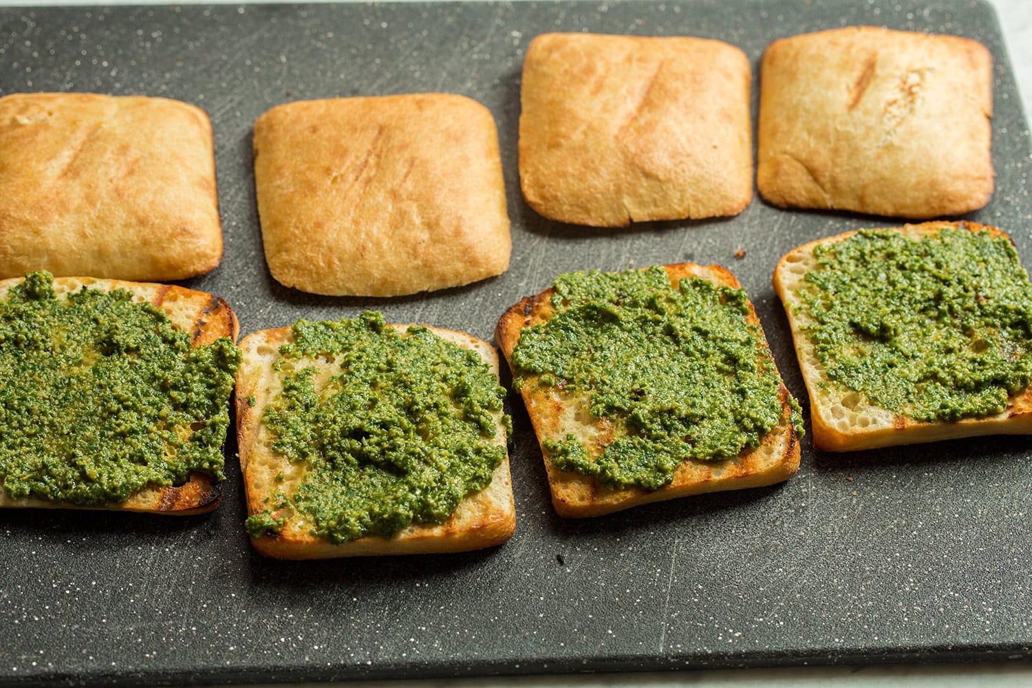 First side of ciabatta spread with homemade pesto.