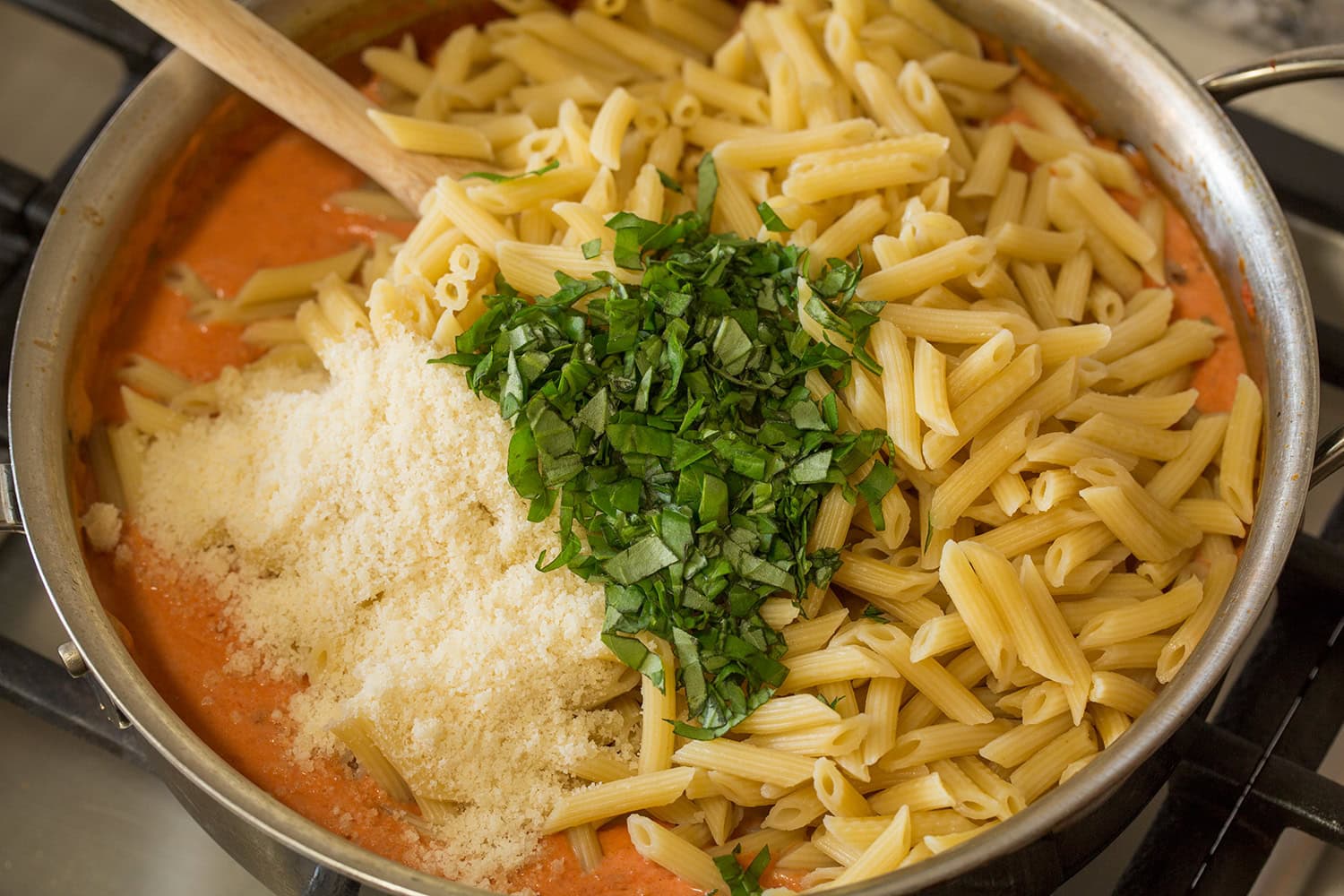 Drained pasta, chopped basil and grated parmesan cheeses added to creamy tomato pasta sauce in saute pan.