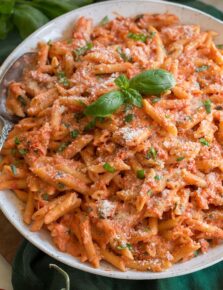 Close up photo of creamy tomato pasta. Shown on penne pasta with basil and parmesan garnish.