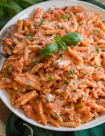 Close up photo of creamy tomato pasta. Shown on penne pasta with basil and parmesan garnish.