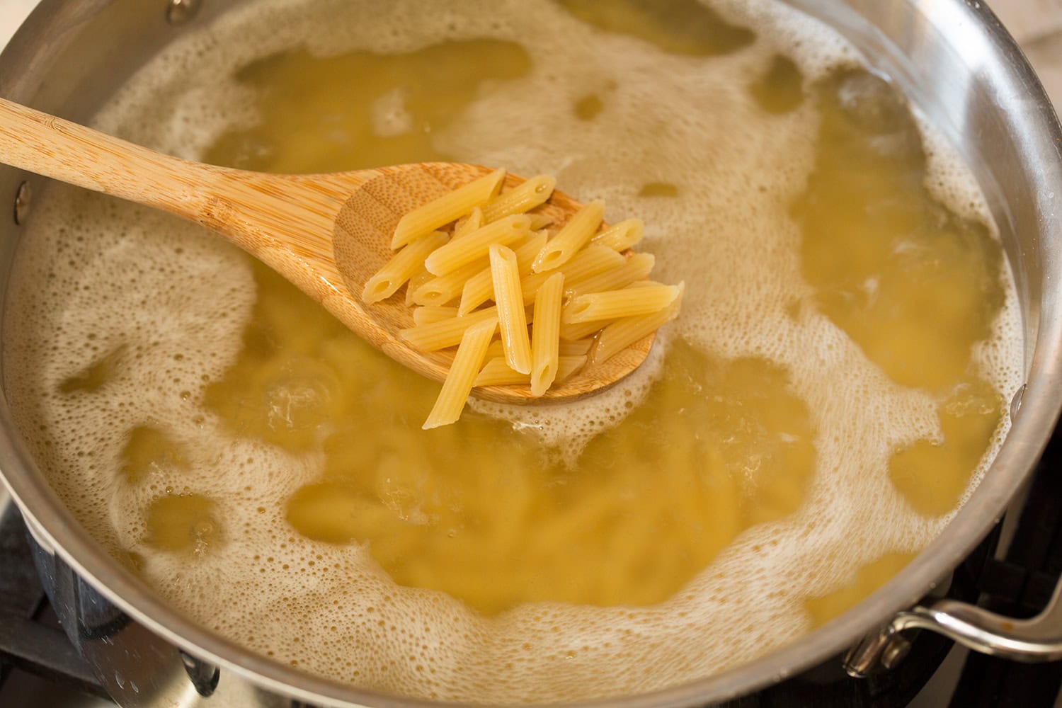 Mini penne pasta shown scooped from a pot onto a spoon.