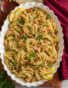Overhead photo of tuna pasta made with spaghetti noodles, canned tuna, capers, and sun dried tomatoes in a scalloped white bowl.