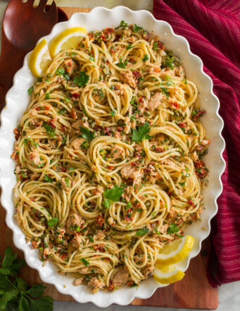 Overhead photo of tuna pasta made with spaghetti noodles, canned tuna, capers, and sun dried tomatoes in a scalloped white bowl.
